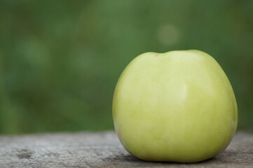 One large beautiful green juicy apple on a wooden board on a green background, in the right part of the photo.