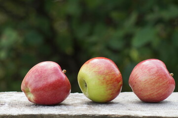 Three large juicy, ripe, beautiful green and red apples in nature on a wooden board.