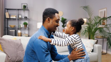 Happy young African American father hugs his cute little daughter tightly. Parental love and care. Carefree childhood.