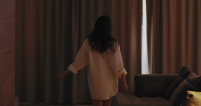 Young woman in hotel room opening window curtain, looking outside feel fresh motivated start new day in modern home