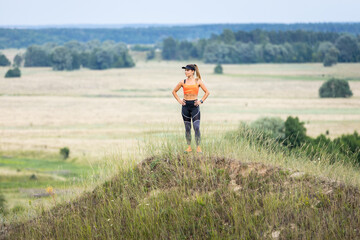 Naklejka na ściany i meble Young sporty runner girl standing on the hill