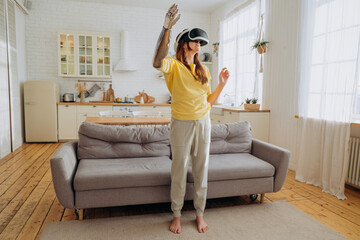 Positive young woman in casual clothes with modern bionic arm and virtual reality headset dances...