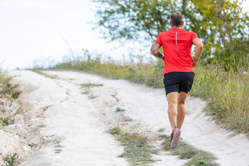 Sporty bearded man running on the path at hillside