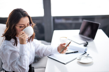 Side View On Attractive Brunette Woman Drinking Coffee And Working On Laptop While Sitting Alone In Restaurant