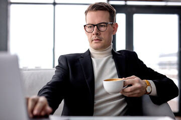 Elegant Businessman In Eyeglasses Sit In Cafe Or Restaurant, In Formal Wear, Working On Laptop Over Cup Of Coffee