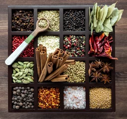 Fotobehang Top down view of a variety of whole spices in a compartment box with a wooden spoon of fennel seeds on top. © Carey