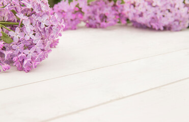 Closeup branches of blooming lilac designed as frame on white wooden background. Space for product or text on foreground. Purple flowers wallpaper