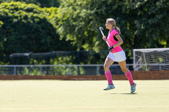 Young girl field hockey player running on pitch
