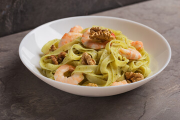 Dish of Tagliatelle pasta with shrimps, pesto sauce, walnut on white plate on dark stone table. Mediterranean cuisine.
