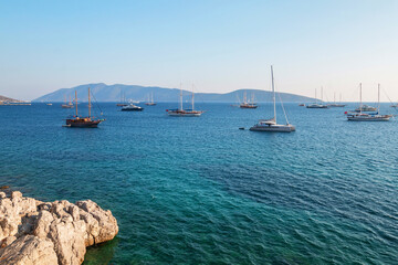 Calm blue sea, rock coast and anchored sail boats. Bodrum, Turkey. Sailing boats in the open sea on a hot summer day at sunset.