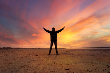 Silhouette of a man with stretched arms on a beach during a colorful sunset