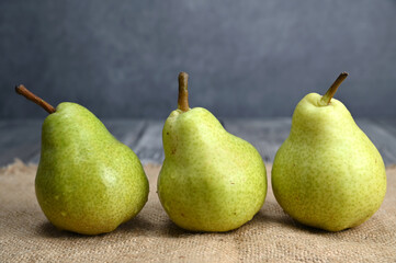 Three green pears of the same sort are standing next to each other on sackcloth