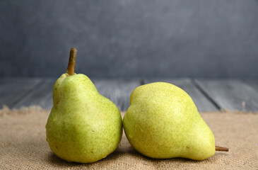 Two green pears of the same variety. One pear stands, another lies nearby on a sacking