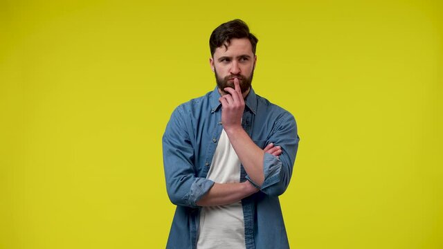 Portrait of a bearded man, thinking intently, putting his hand on his chin, raising his index finger, an idea arose. A man in the studio on a yellow background. Close up. Slow motion ready 59.97fps.