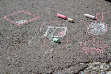Coloured chalks over children's drawings on the asphalt pavement