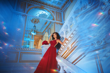 Beautiful brunette girl in a red ball gown on the background of white and gold palace interiors