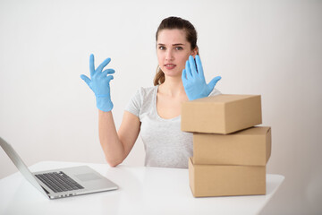a European woman with blue gloves sits behind boxes next to a laptop