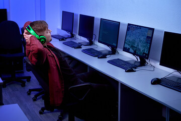 The happy guy leans on the back of the chair, hands behind his back and rests. Computer class.