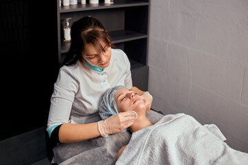 Obraz premium Professional facial skin care in a beauty salon. Mechanical cleaning of the face with cotton pads. Cleansing the face of a young female client.