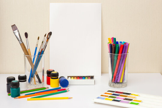White paper, paintbrushes and colorful drawing supplies on white table. Mock up