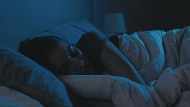 Trouble sleeping. Night insomnia. Bedtime fatigue. Disturbed tired woman lying in bed with closed eyes late in dark home bedroom with blue light.