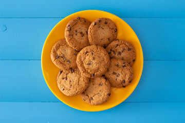 Chocolate chip cookies on a yellow plate over ocean blue wooden table