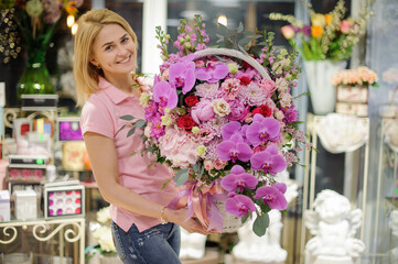 large white wicker basket with different pink flowers in hands of young woman florist