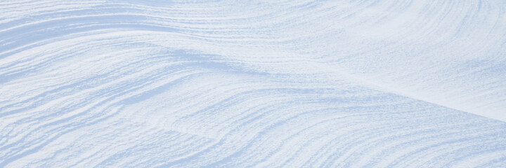 Beautiful winter background with snowy ground. Natural snow texture. Wind sculpted patterns on snow surface. Wide panoramic texture for background and design.