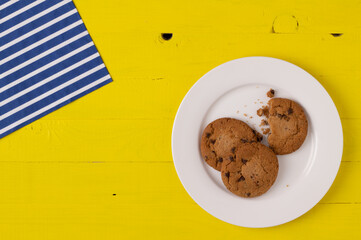 Chocolate chip cookies on a white porcelain plate over yellow wooden table