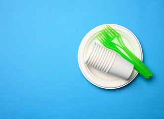 green plastic forks and empty white paper disposable plates on a blue background,