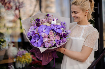 happy woman with beautiful bouquet of purple orchids and lilacs and roses in her hands
