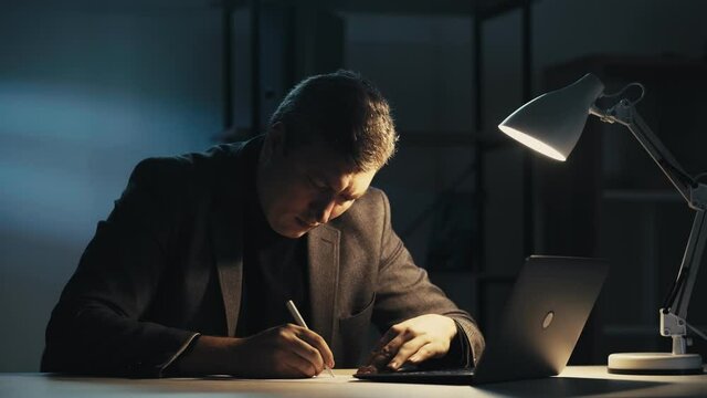 Overwork burnout. Night stress. Late work anxiety. Tired annoyed male entrepreneur working dissatisfied with writing ideas creasing throwing away paper at dark home office workplace with laptop.