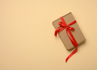 rectangular brown cardboard box tied with a silk red ribbon on a beige background, top view