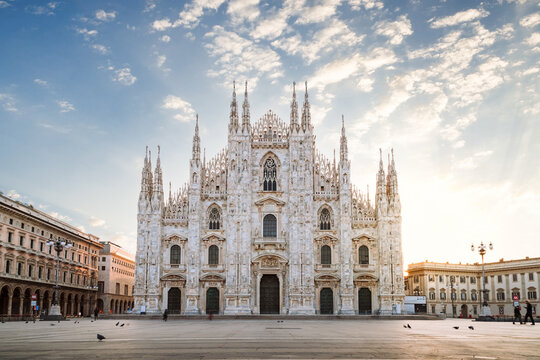 View of the Milan Cathedral with empty square due to the coronavirus blockade, with blue sky with white clouds and glow of light from the newly risen sun