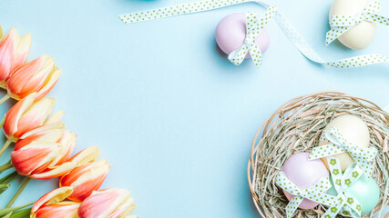 Easter flat. Colorful egg with tape ribbon, spring tulips, feathers on pastel blue background in Happy Easter decoration. Spring holiday top view concept.