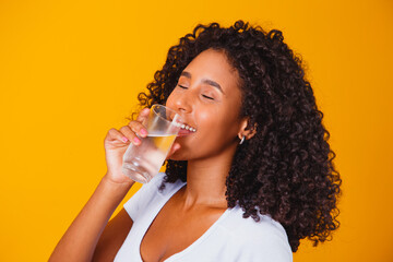 young black woman drinking water in yellow background. Young girl with glass of water