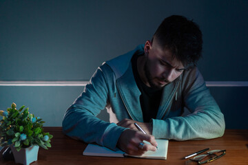 Young concentrated man writing a book in low light environment