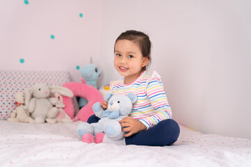 Cute toddler girl in her room sitting on the bed. 