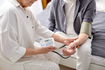Close up of senior woman checking husband's blood pressure with electric monitor at home, copy space