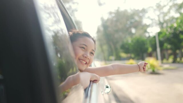 Happy Asian family enjoy and having fun together with outdoor lifestyle activity on road trip vacation. Little child girl kid sit in the car with pull her face and hand out of car window in summer day