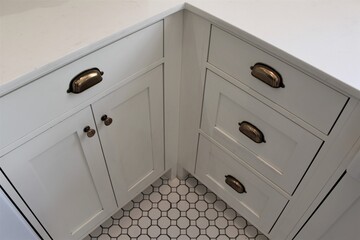 Corner kitchen with white countertop and cabinets and textured tile floors. Small vintage bronze handles for opening and closing the doors. Farm house styled.