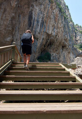 A vertical rear view of a woman bringing backpack climbing up on wooden stairs with rocky background