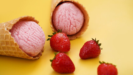 Strawberry ice cream in a waffle cone. Ice cream and berries on a yellow
