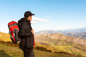 hiker with backpack and hat takes a break to observe the beautiful mountainous landscape. young mountaineer meditating. mountain activities.