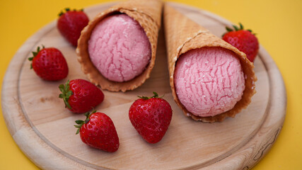 Strawberry ice cream in a waffle cone. Ice cream and berries on a yellow