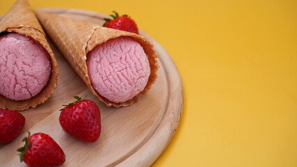 Strawberry ice cream in a waffle cone. Ice cream and berries on a yellow