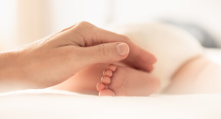 Fototapeta na wymiar Child care love and support. Mothers hand touching teeny baby feet 
