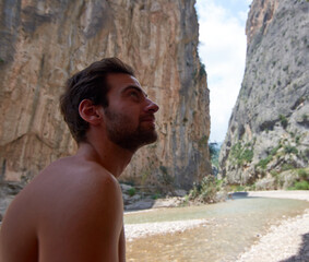 A closeup of a half-naked Caucasian man looking up with a stone wall background