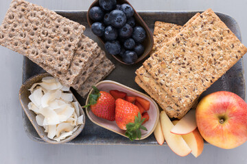 Two piles of crunchy crackers next to three trays full of healthy fruit over an elegant big tray.