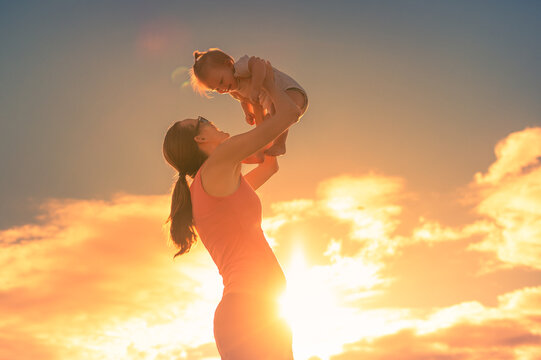 Happy mother holding up her little baby girl to the sunset sky. Family lifestyle and parenting concept. 